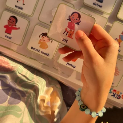A girl holding a “sit” card from the English daily actions cards in My Words